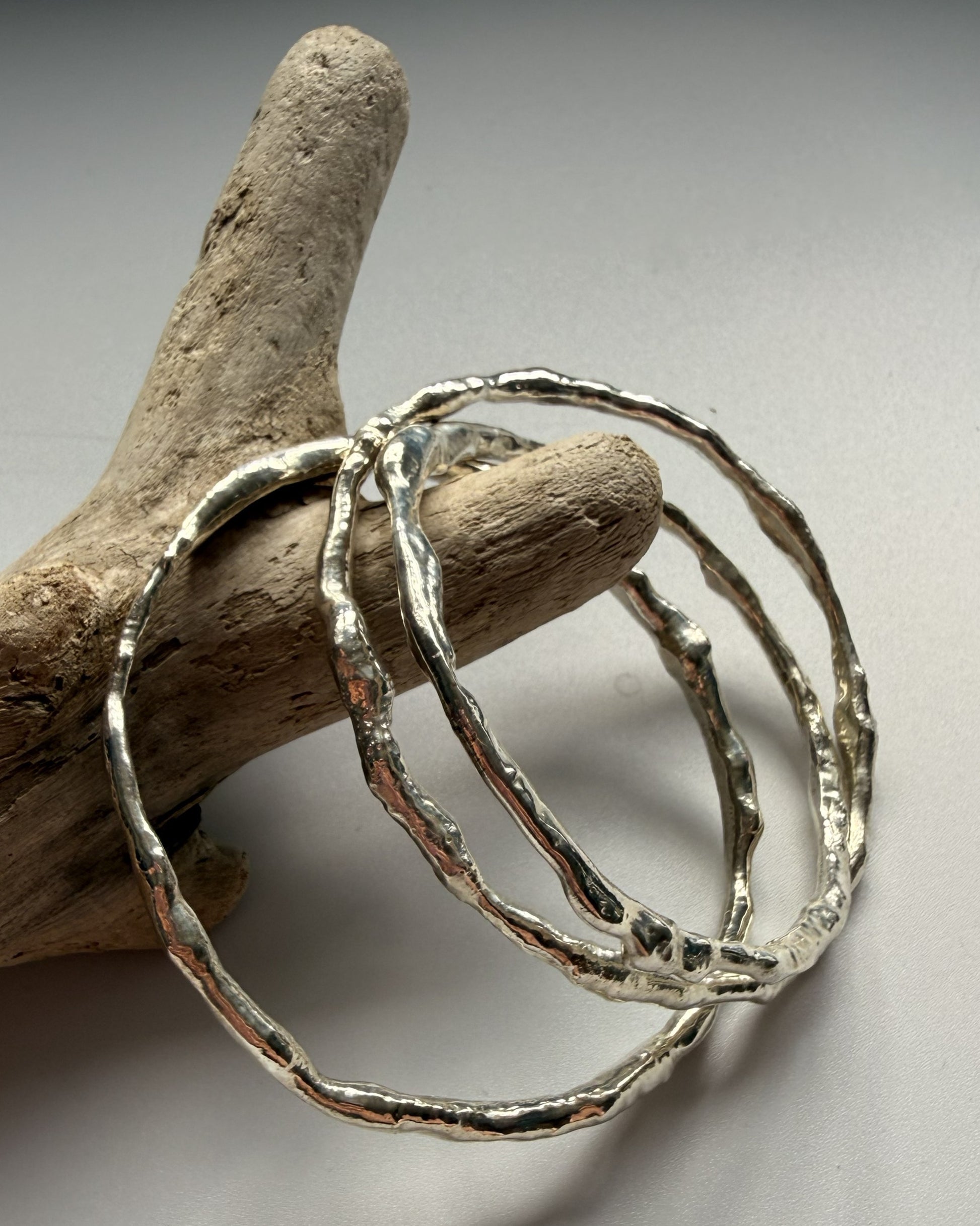 Silver bangles on a piece of driftwood against a neutral background