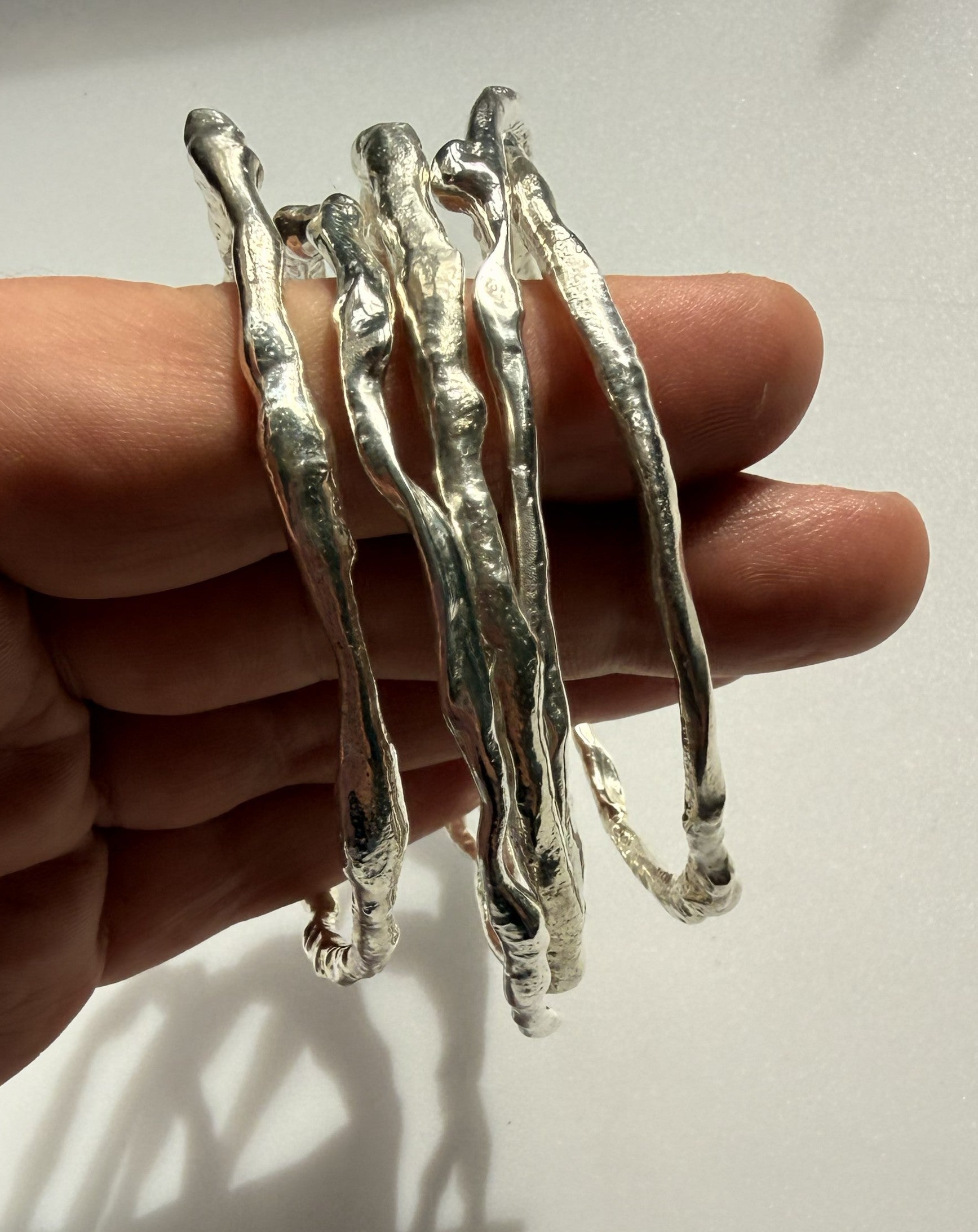 Silver branch-like bracelet held on a hand against a light background