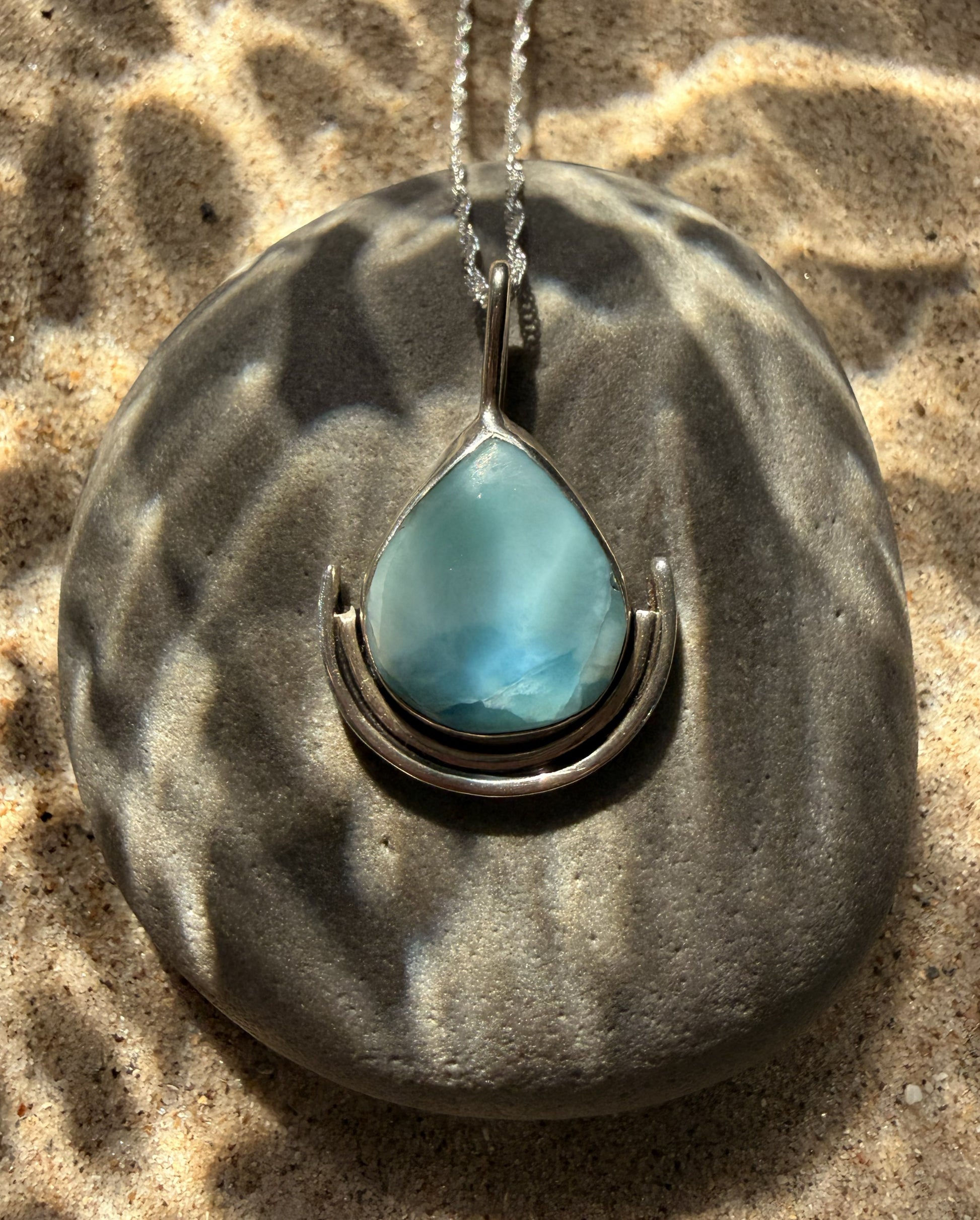 Turquoise larimar teardrop pendant on a silver chain resting on a textured stone surface.