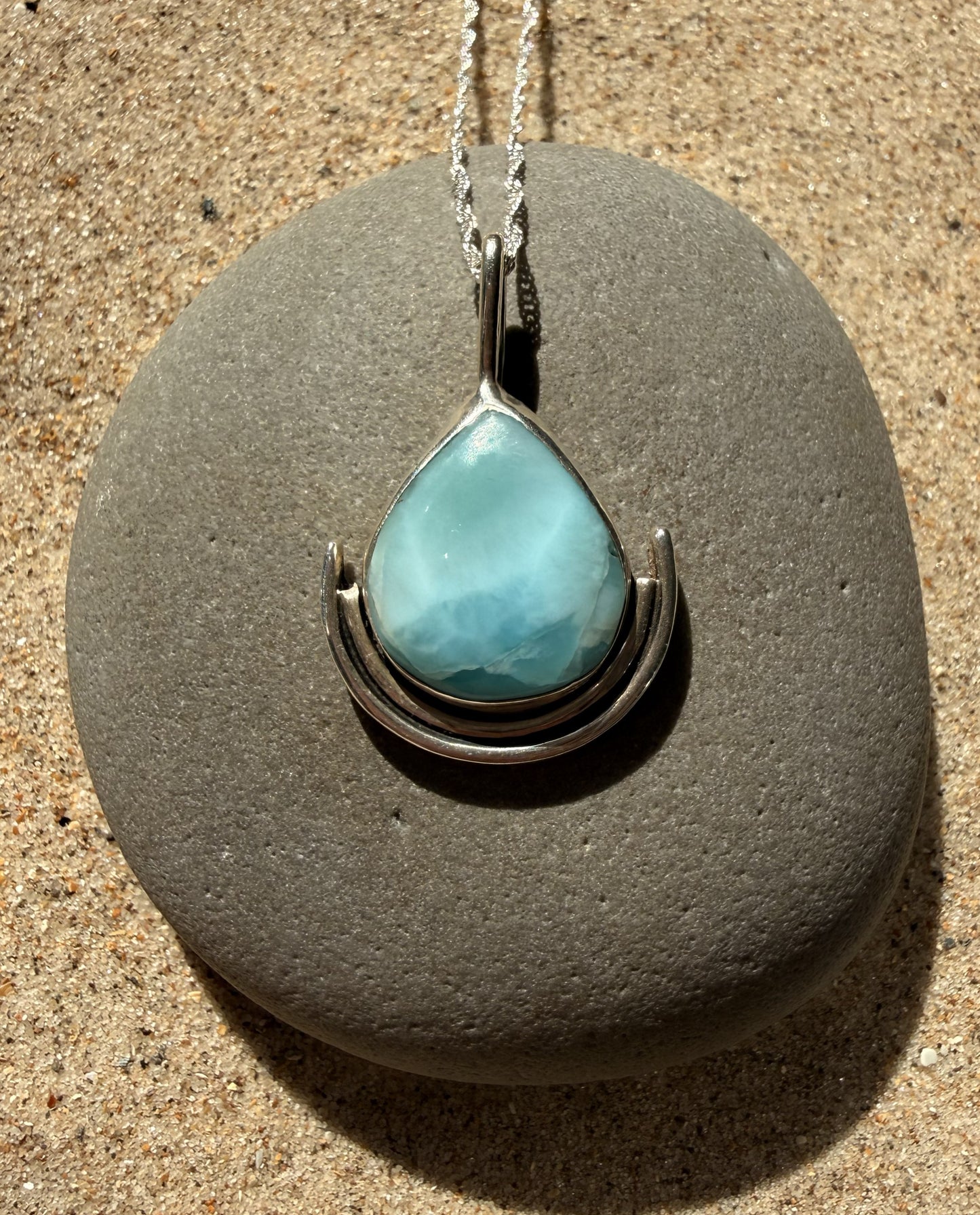 Turquoise teardrop larimar pendant on a silver chain resting on a grey stone.