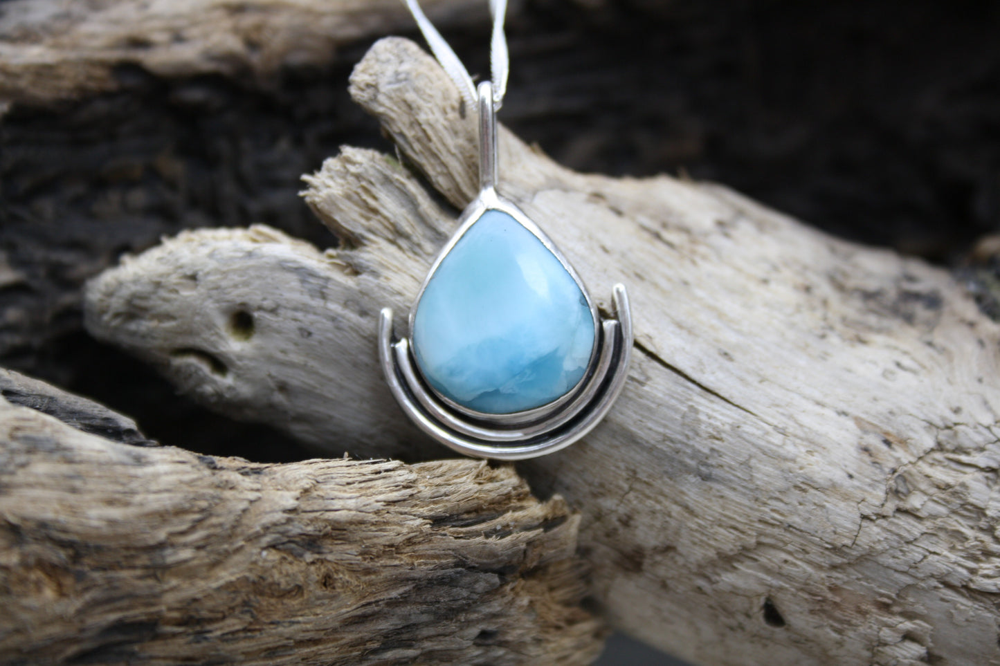 Teardrop-shaped turquoise larimar pendant on silver chain against a wooden background