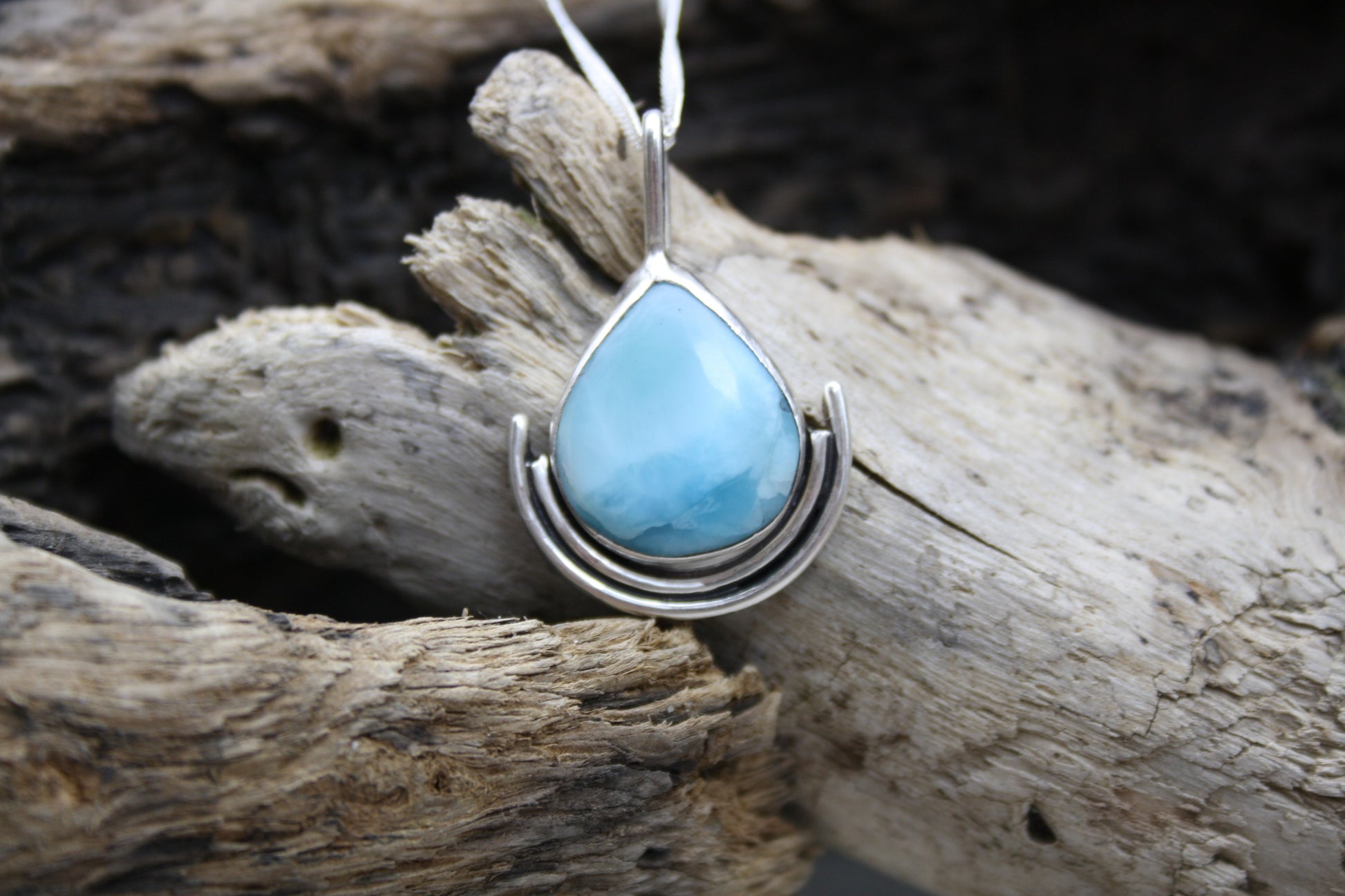 Teardrop-shaped turquoise larimar pendant on silver chain against a wooden background