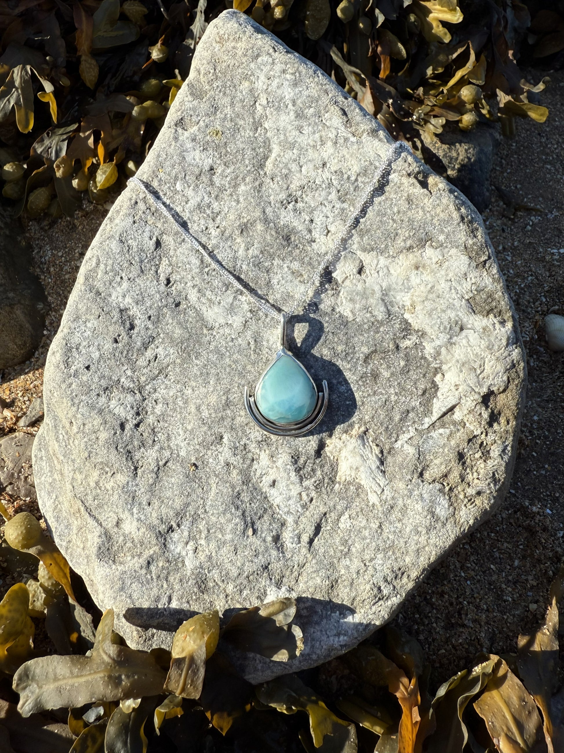 Turquoise larimar pendant necklace on a stone with seaweed in the background