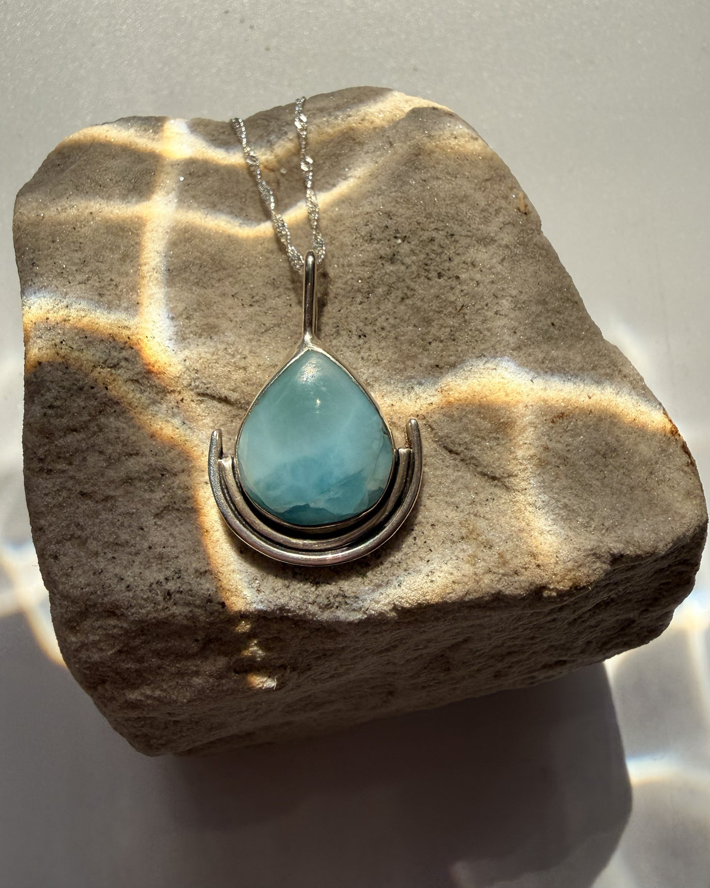 Turquoise larimar teardrop pendant on a silver chain resting on a stone surface.