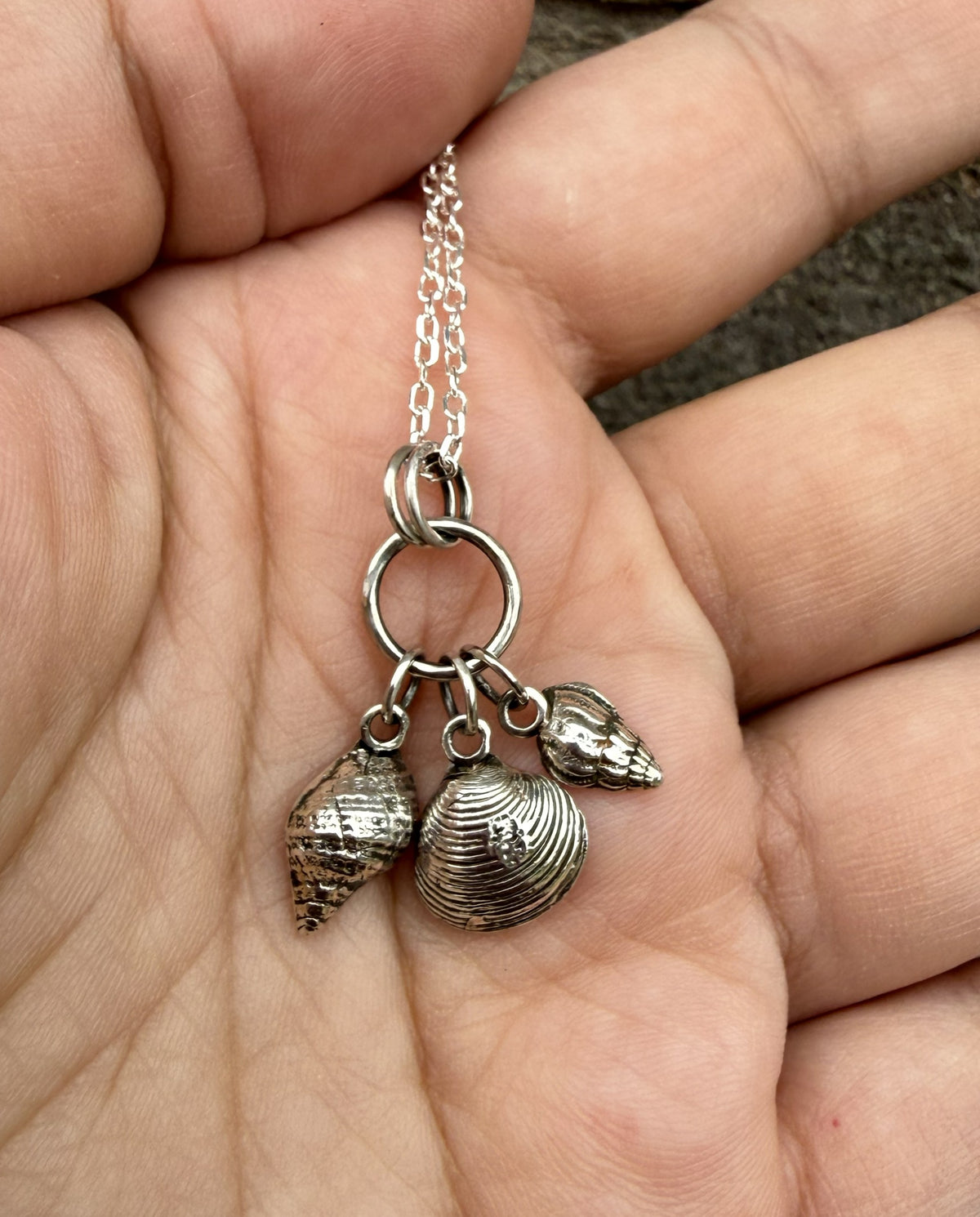 A close-up of a person's hand holding a silver charm necklace with three seashell pendants.