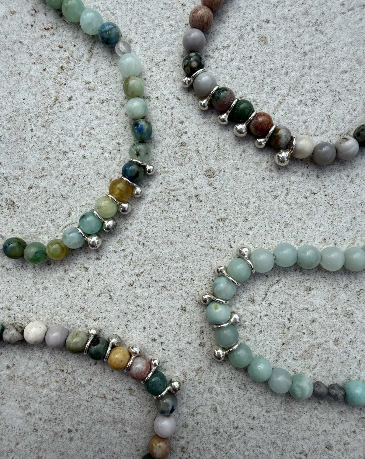 Several beaded silver necklaces with round gemstone beads and small silver spacer beads arranged on a light grey textured surface.