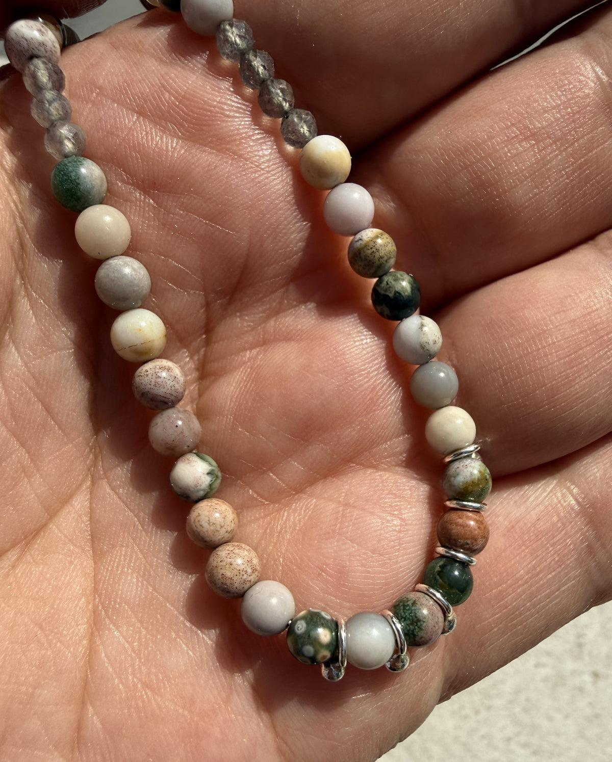 close up of an ocean jasper beaded necklace with silver details, resting on a persons palm