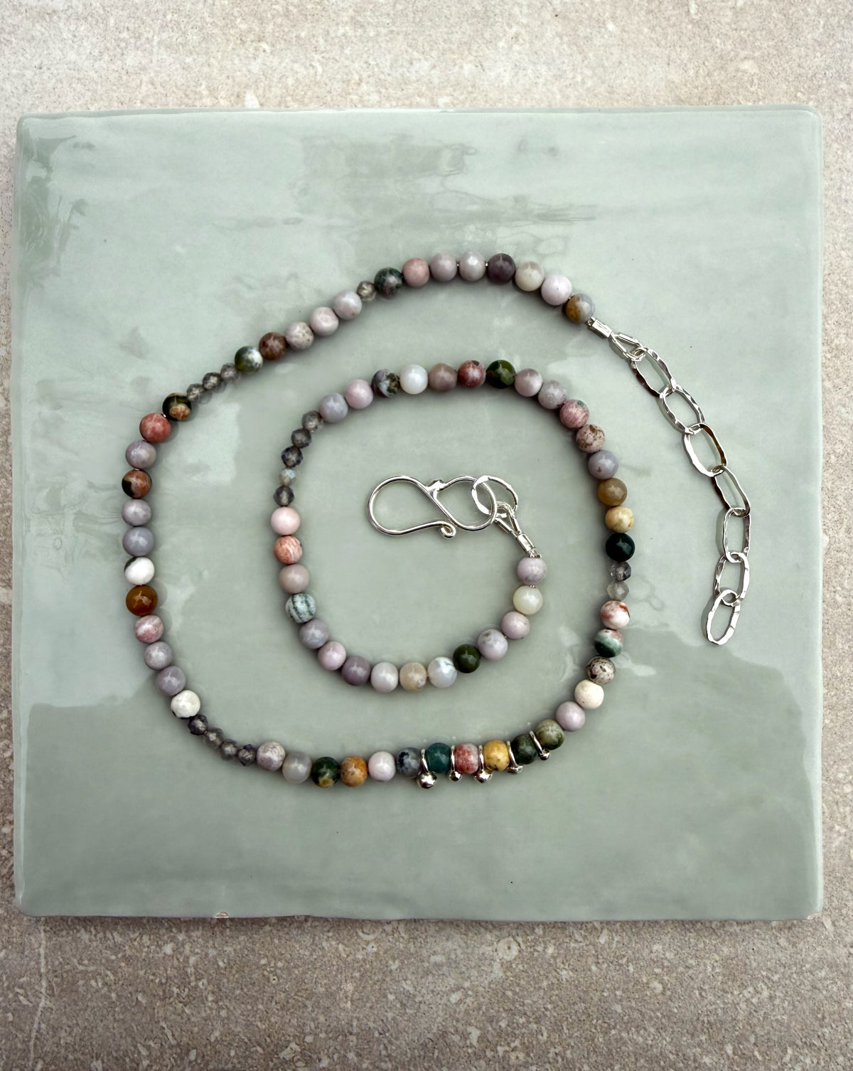 Ocean Jasper beaded silver necklace, curled in a spiral on a pale green tile